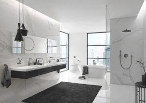 Biała łazienka z 2 umywalkami po lewej i prysznicem z deszczownicą po prawej; z tyłu stoi wanna i duże okno.