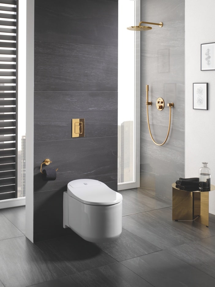 Łazienka w odcieniach szarości z toaletą ze złotym przyciskiem spłukującym i złotym zestawem prysznicowym