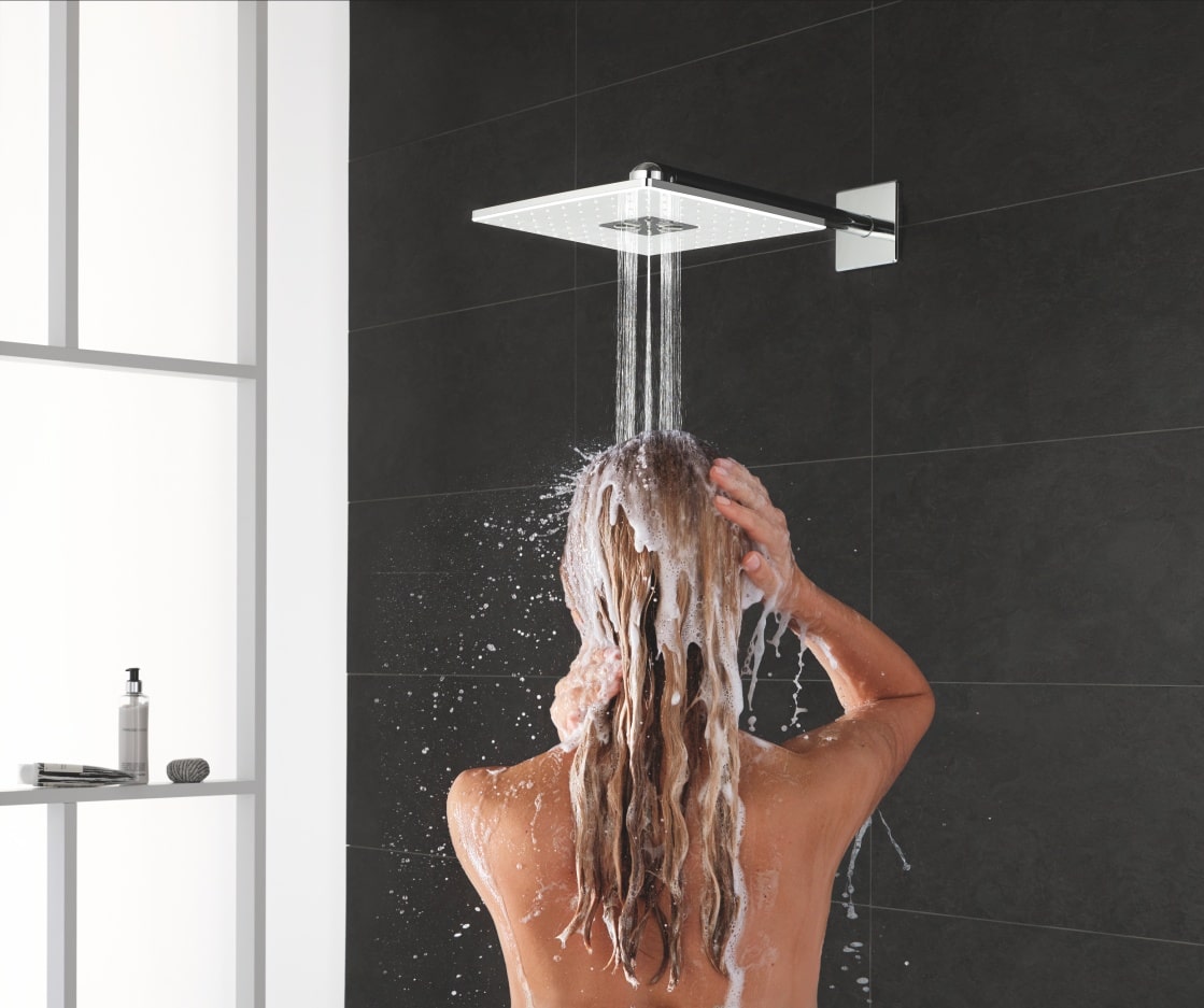 Kobieta spłukuje szampon z włosów, stojąc pod deszczownicą